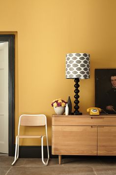 a room with yellow walls and a white chair next to a lamp on top of a dresser