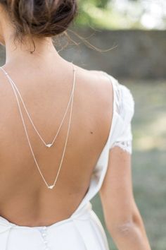 the back of a woman's white dress with two necklaces on her neck