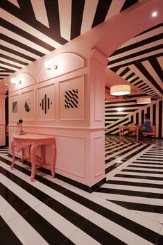 a room with black and white stripes on the walls, pink tables and stools