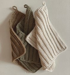 three knitted dishcloths hanging from hooks on a white wall, one is green and the other is brown