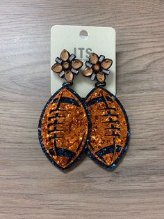 an orange and black pair of earrings with flowers on it, sitting on top of a wooden