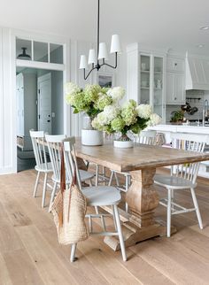 a dining room table with white chairs and flowers in vases