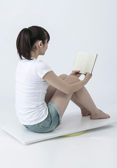 a woman sitting on top of a white surface with a book in her lap and legs crossed