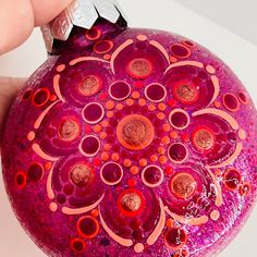 a hand holding a purple and red ornament with circles painted on the top