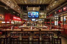 the inside of a restaurant with many tables and stools, television in the background