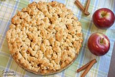 an apple pie on a table with apples and cinnamon sticks