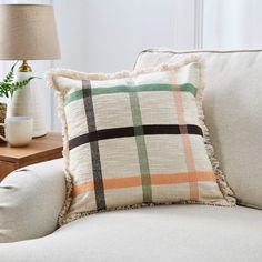 a plaid pillow sitting on top of a white couch next to a table with a lamp