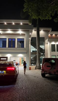 two cars parked in front of a large white building with lights on it's windows