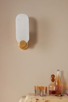 a wooden table topped with glasses and bottles next to a wall mounted light on the wall