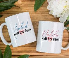 two coffee mugs sitting on top of a wooden table next to flowers and leaves