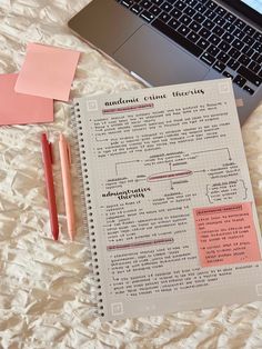 an open notebook sitting on top of a bed next to a laptop computer and pen