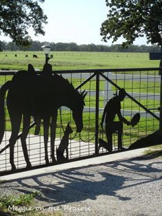 the silhouettes of people and horses are behind a fence that has a dog on it