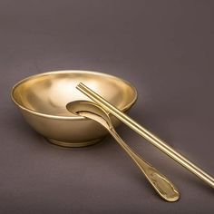 two gold colored bowls with spoons in them on a gray surface, one is empty