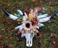 an animal skull with flowers and feathers on it's head sits in the grass