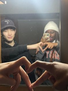 two hands making the shape of a heart in front of a mirror with another person taking a selfie