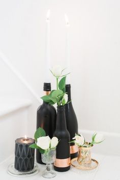 several bottles with flowers in them sitting on a table next to candles and wine glasses