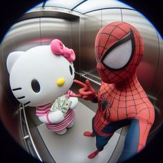 a hello kitty doll is standing next to a spider - man in a bathroom mirror