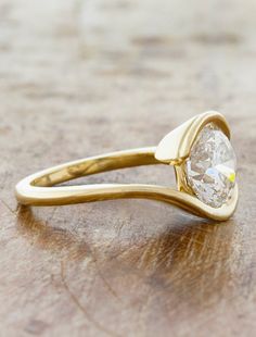 a yellow gold ring with a pear shaped diamond in the center on a wooden surface