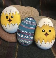 three painted eggs sitting next to each other on top of a stone covered ground with rocks