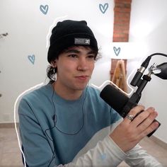 a man sitting in front of a microphone with headphones around his neck and wearing a beanie