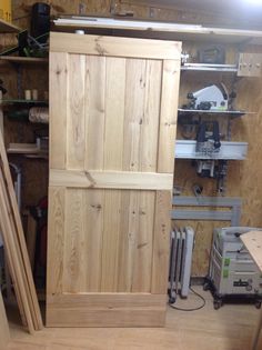 a large wooden door sitting inside of a room next to a shelf filled with tools