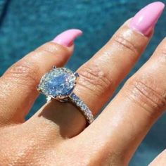 a close up of a person's hand with a ring on their finger and an ocean in the background