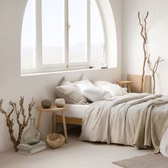 a bedroom with white walls and large arched window, bed in foreground is made up with linens