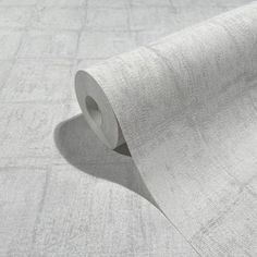 a roll of grey fabric on top of a white tablecloth with a shadow from the floor