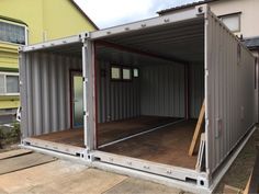 an empty shipping container is shown in front of a yellow and gray building with its doors open