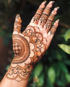 a woman's hand with henna tattoos on it and green leaves in the background