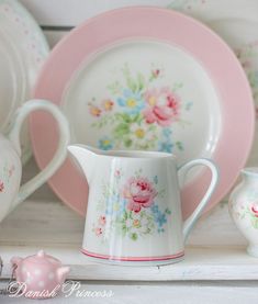 a pink and white china set on a shelf with other plates, cups and saucers