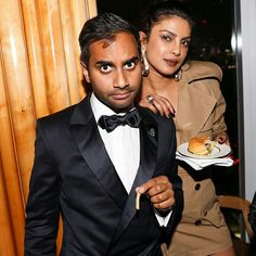 a man in a tuxedo holding a plate with a sandwich on it while standing next to a woman