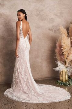 a woman in a white wedding dress standing next to a vase with dried flowers on it