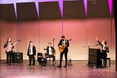 a group of young men standing on top of a stage playing guitars and singing into microphones