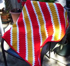 a crocheted blanket sitting on top of a chair next to a potted plant