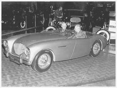 an old black and white photo of two men in a sports car with the driver behind them