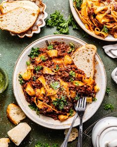 two plates filled with pasta and bread on top of a green tablecloth next to silverware