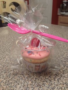 a cupcake with pink frosting and a toothbrush in its plastic wrapper