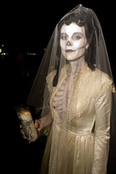 a woman dressed up as the bride holding a candle in her hand and wearing a veil