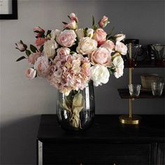 a vase filled with pink and white flowers sitting on top of a wooden table next to a shelf