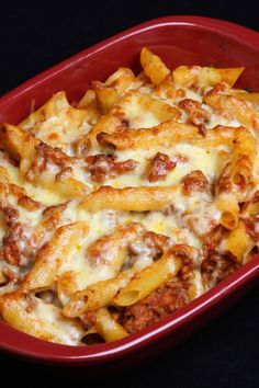 a red casserole dish filled with cheesy pasta and meat covered in sauce