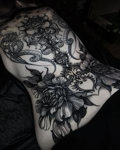 a woman's back with black and white tattoos on her body, flowers in the middle