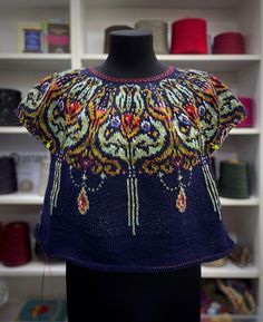 a mannequin wearing a blue top with colorful designs on it's shoulders