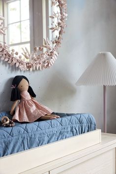 a doll sitting on top of a blue bed next to a lamp and a mirror