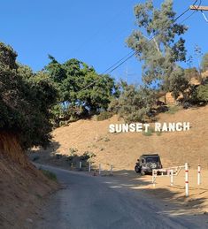 a truck is parked on the side of a dirt road next to a sign that says sunset ranch