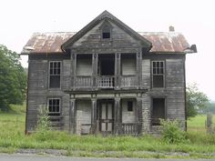 an old run down wooden house in the middle of a field with grass and trees