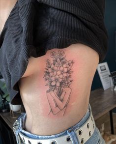 a woman's stomach with flowers in her hand tattoo on the back of her body