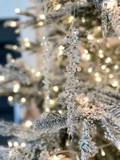 a white christmas tree with snow flakes on it's branches and lights in the background