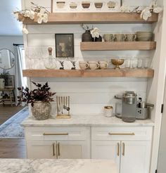 a kitchen with white cabinets and marble counter tops, gold accents on the upper shelves