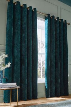 a living room with green velvet curtains and a blue rug in front of the window